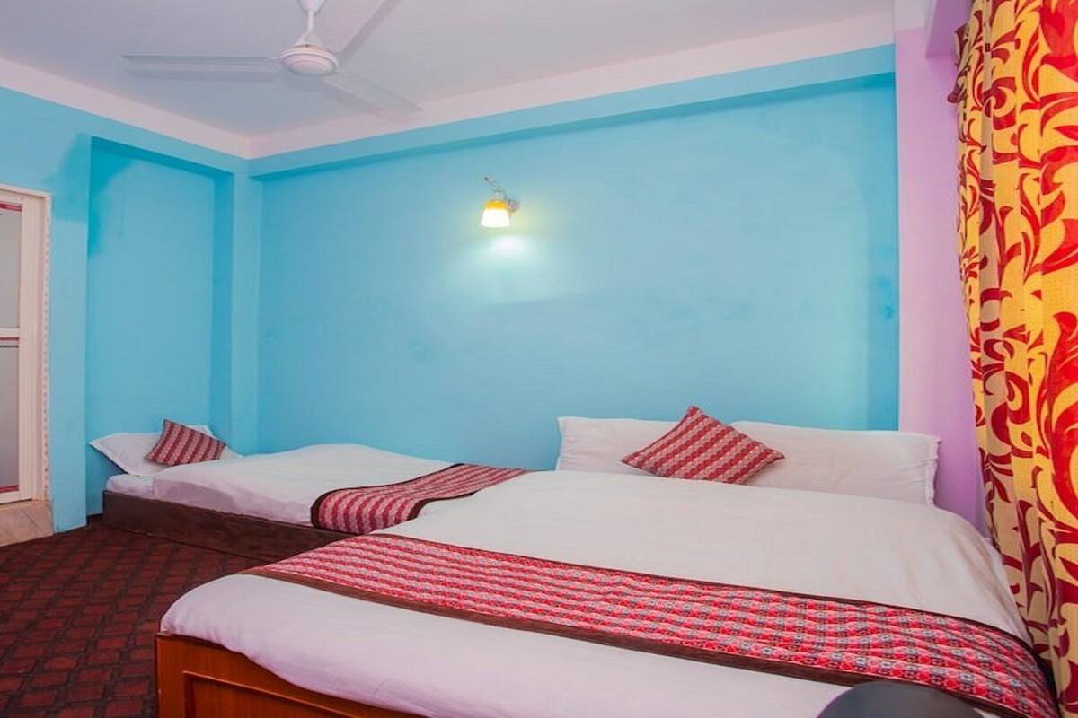 A room with two beds, a ceiling fan, a wall-mounted light, and a door with a window.