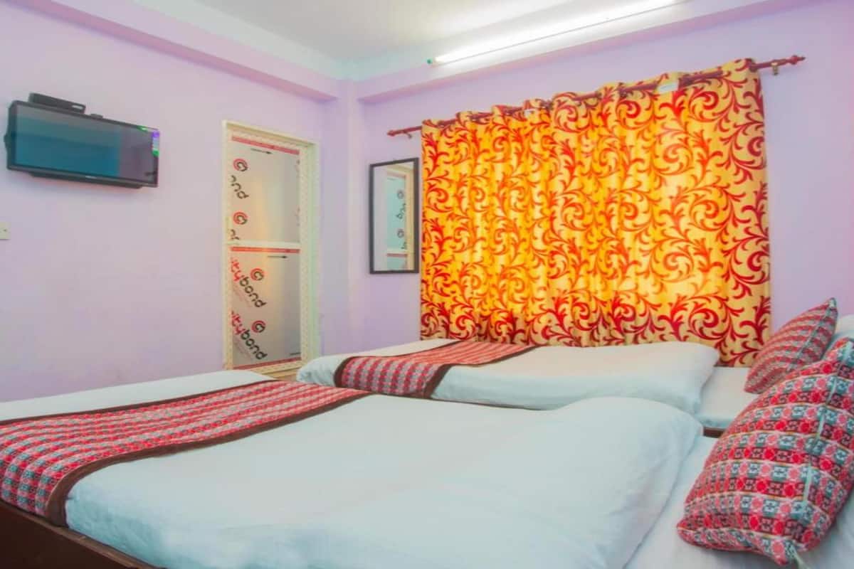 A hotel room with two beds, a television on the wall, and a patterned curtain.