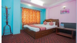 Un dormitorio con una cama, cabecera de madera, mesita de noche y televisor instalado en la pared.