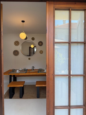 A dining area with a wooden table, benches, a hanging light fixture, and a mirror on the wall. - Cozy villa 5 min from the beach (Lignano Sabbiadoro)