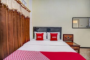 A hotel room with a bed, two red pillows with "OYO" text, a wooden nightstand, and a mirror on the wall. - Hotel O Lancar Homestay Syariah (Batu)