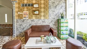 A lobby with a patterned wall, a brown leather sofa, a coffee table with a vase of flowers, and a green toy storage unit. - Hotel O Lancar Homestay Syariah (Batu)