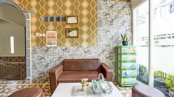 A lobby with a patterned wall, a brown leather sofa, a coffee table with a vase of flowers, and a green toy storage unit.