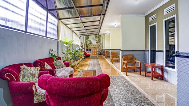 A spacious indoor area with a red sofa set, wooden chairs, a tiled floor, and a staircase leading to an upper level. - Hotel O Lancar Homestay Syariah (Batu)