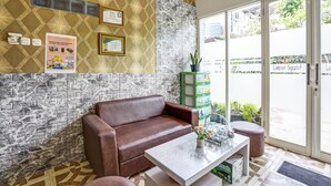 A reception area with a brown leather sofa, a glass-top table with a vase, and a patterned wall with certificates. - Hotel O Lancar Homestay Syariah (Batu)