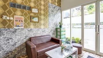 A reception area with a brown leather sofa, a glass-top table with a vase, and a patterned wall with certificates.