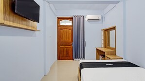 A bedroom with a bed, a TV mounted on the wall, a wooden dresser, a mirror, and an air conditioning unit. - OYO Life  91947 Kost Barokah Syariah (Mojokerto)