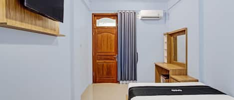 A bedroom with a bed, a TV mounted on the wall, a wooden dresser, a mirror, and an air conditioning unit.
