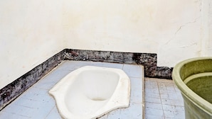 A small, tiled bathroom with a white toilet and a green bucket. - OYO Life  91947 Kost Barokah Syariah (Mojokerto)