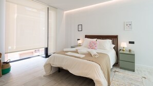Un dormitorio moderno con una cama grande, mesitas de noche con lámparas, una ventana con persianas y vistas al exterior.
