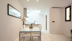 Una cocina moderna con comedor, que incluye una mesa de vidrio, sillas blancas y vistas a la cocina a través de una puerta abierta.