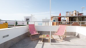 Una terraza en la azotea con dos sillones a rayas, una mesita con bebidas y una vista despejada del horizonte de la ciudad.