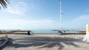 Un paseo marítimo con vista despejada al mar, un farol alto y algunas personas caminando.
