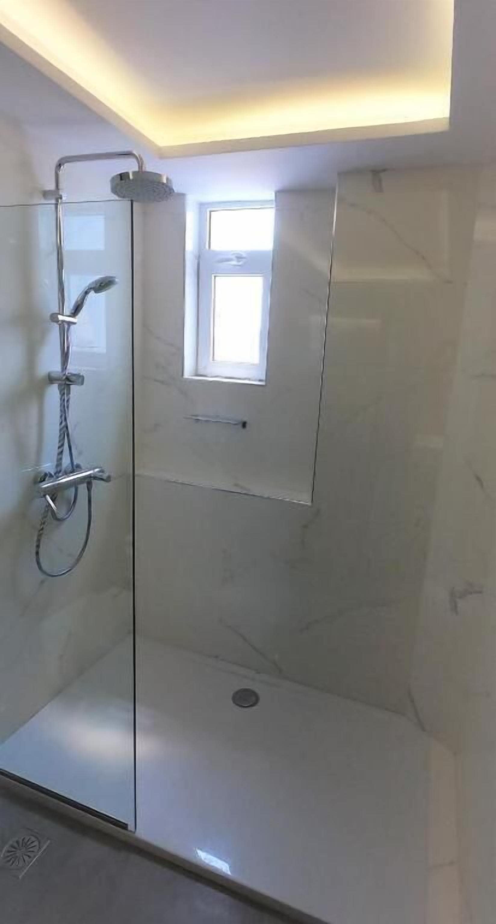 Een moderne douche met een glazen deur, een klein raam en een marmeren wand.