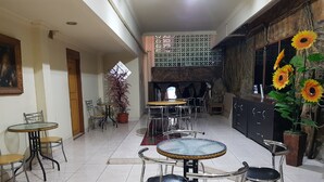 A dining area with round tables and chairs, a potted plant, and a wall with a decorative pattern. - Hotel O Istana (Makassar)