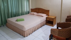 A neatly made bed with a green towel, a wooden nightstand, and a wicker chair. - Hotel O Istana (Makassar)