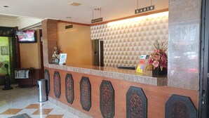 A reception desk with a nameplate, a reception area, and a wall-mounted television. - Hotel O Istana (Makassar)