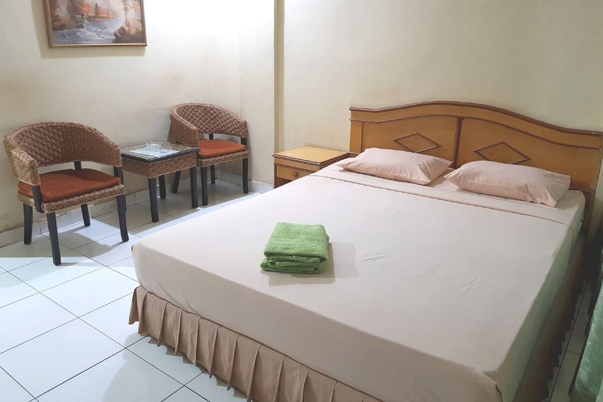 Une chambre à coucher bien rangée, avec un lit, deux fauteuils en osier, une petite table et une table de chevet.