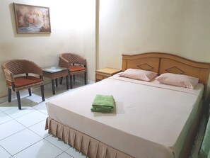 Une chambre à coucher bien rangée, avec un lit, deux fauteuils en osier, une petite table et une table de chevet.