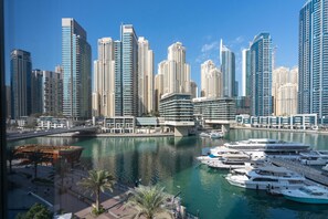 A marina with multiple yachts docked, surrounded by high-rise buildings and a clear blue sky.