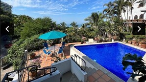 Un área de piscina con piscina azul, sillas de descanso y sombrillas.