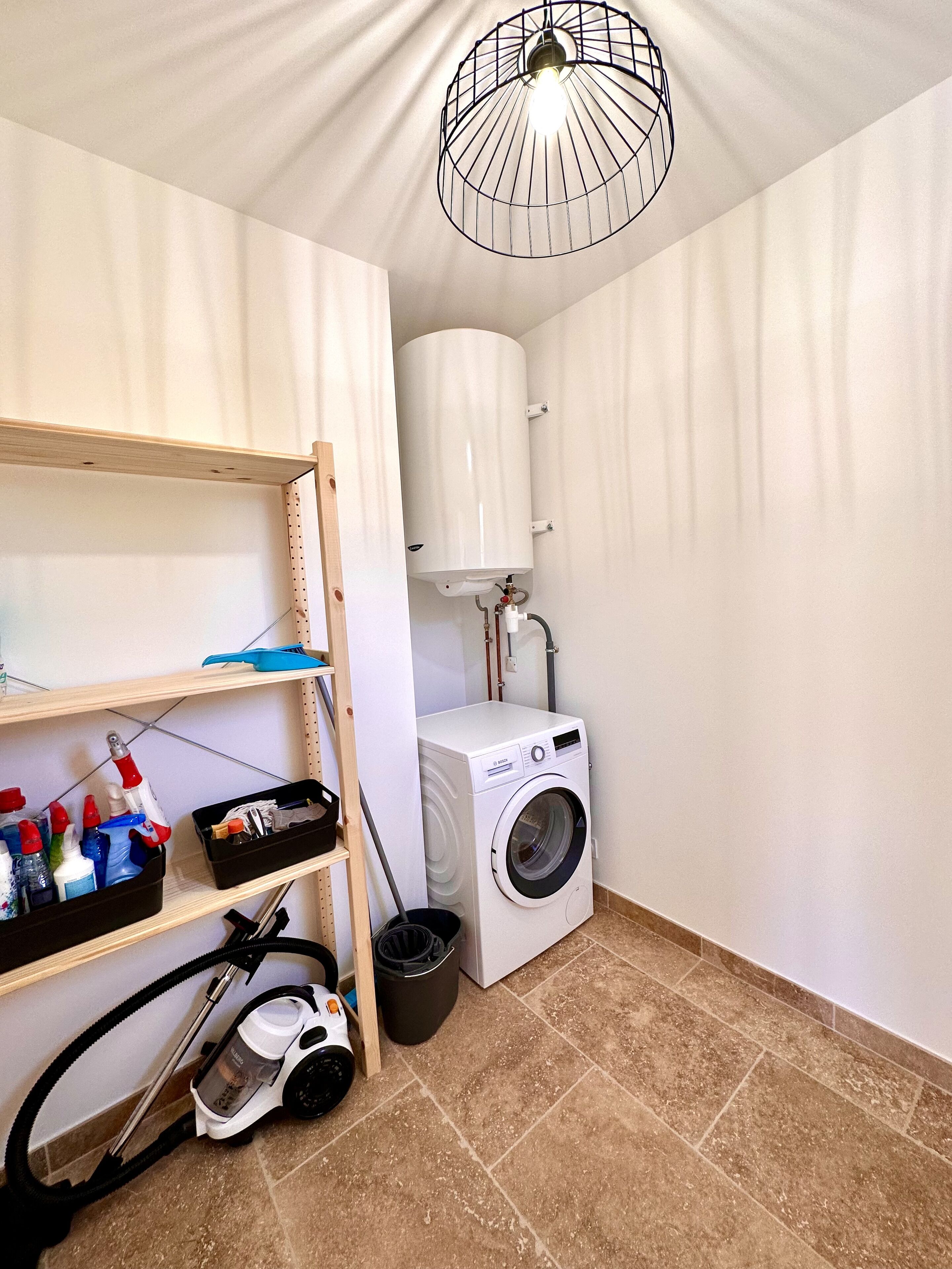 A laundry room with a washing machine, a ceiling light fixture, and a shelf with cleaning supplies.