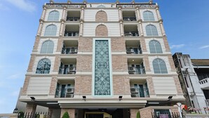 Un hotel de varios pisos con un elemento vertical central, balcones y un vehículo en la entrada.