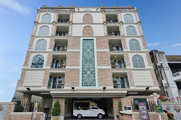 Hotel de diverses plantes amb un element vertical central, balcons i un vehicle a l'entrada.