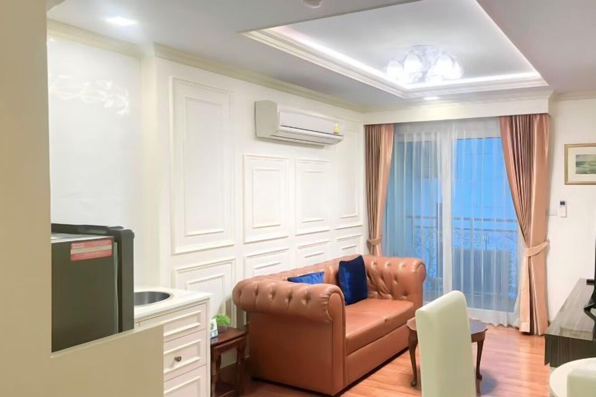 Una sala de estar con un sofá de cuero marrón, una mesa de comedor y un ventanal con cortinas traslúcidas.