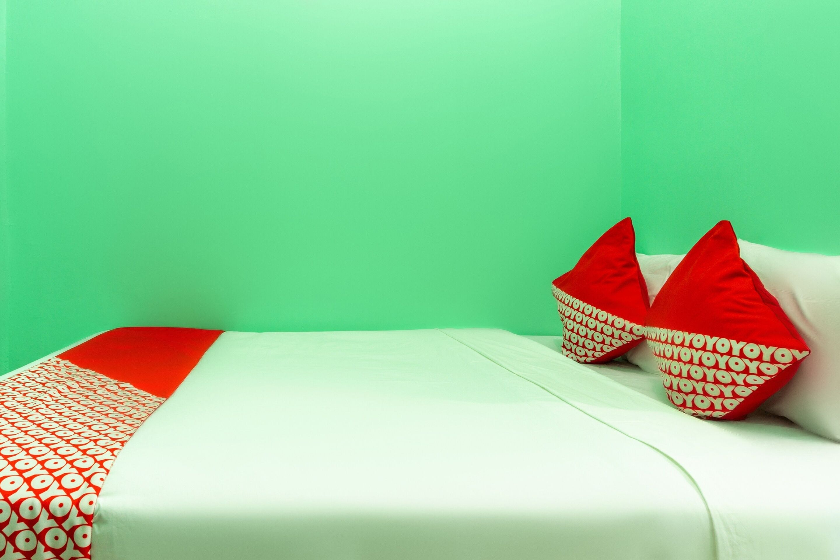A bed with a red and white patterned bedspread and two red pillows with white text.