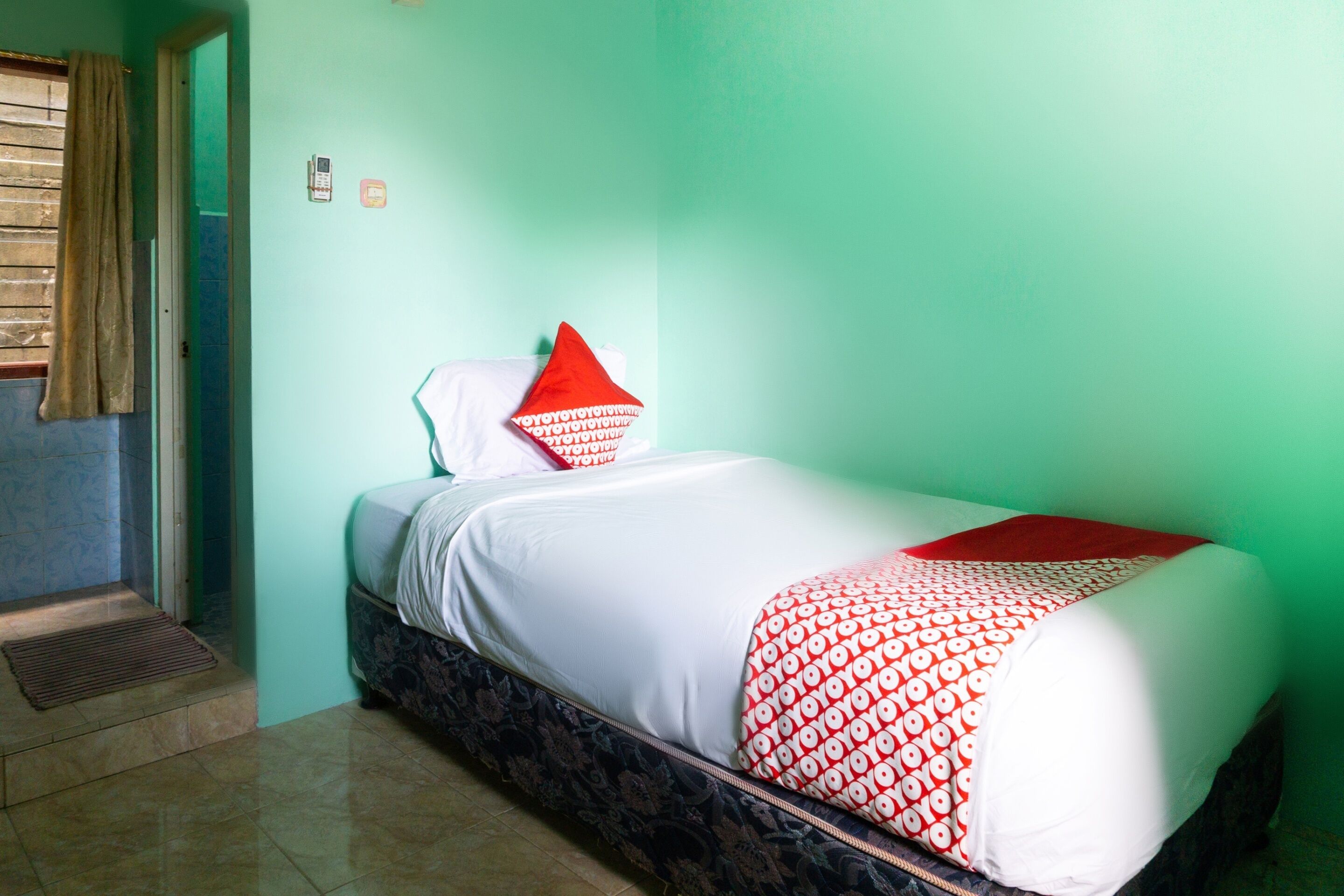 A single bed with a patterned bedspread, a red pillow, and a white pillow.