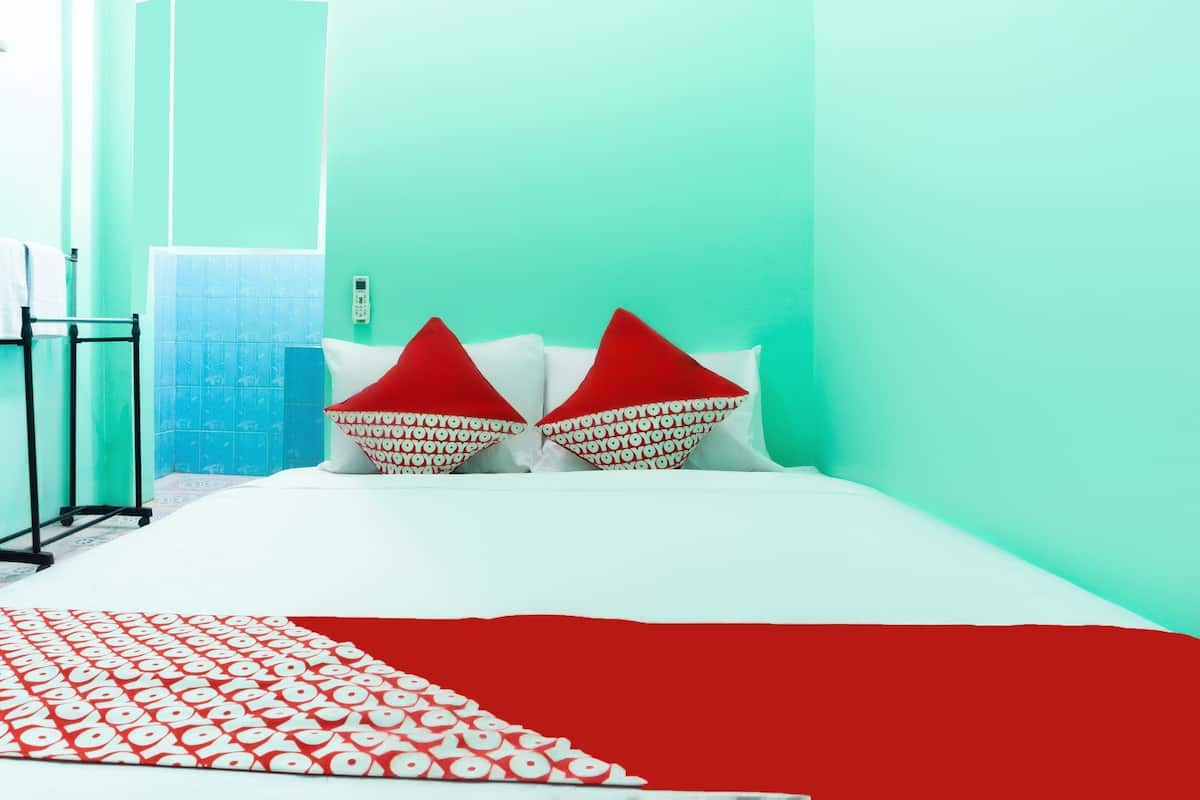 A room with teal walls, a white bed, red and white patterned pillows, and a red and white patterned blanket.