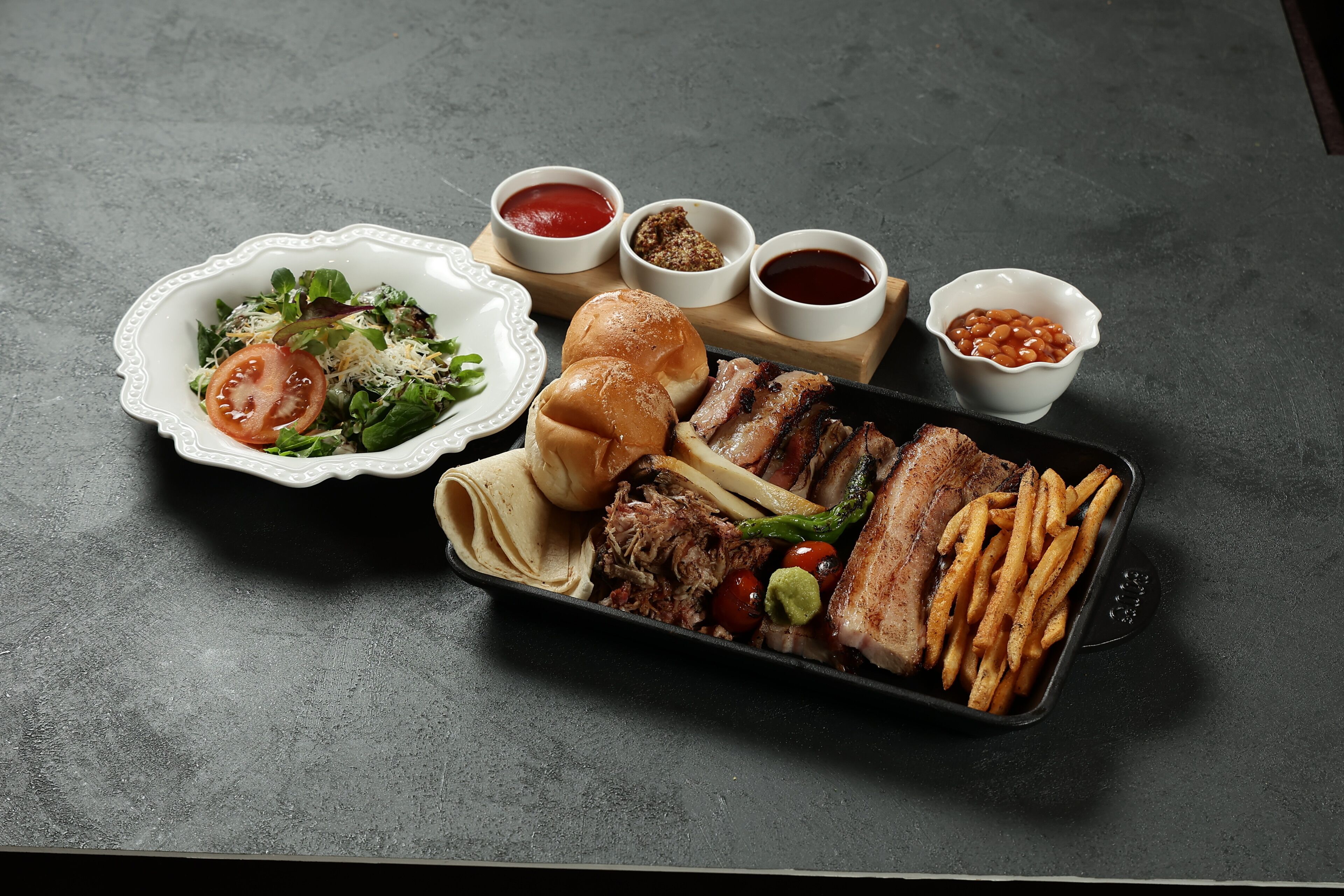 A meal with a salad, burger, ribs, and fries on a dark surface.