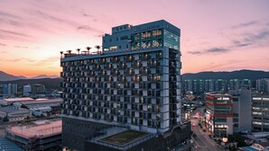 A modern hotel with multiple floors, a rooftop garden, and a view of the cityscape at dusk.
