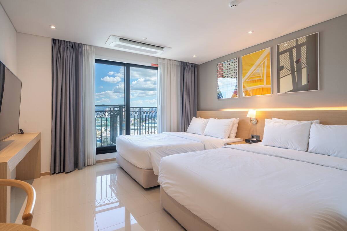 Een hotelkamer met twee bedden, een bureau, een stoel, een televisie en een balkon met uitzicht.