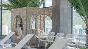 A sunlit indoor lounge area with white lounge chairs, a seating area with cushions, and a decorative screen with arches.