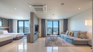A modern hotel room with a bed, sofa, TV, and a balcony with a view.