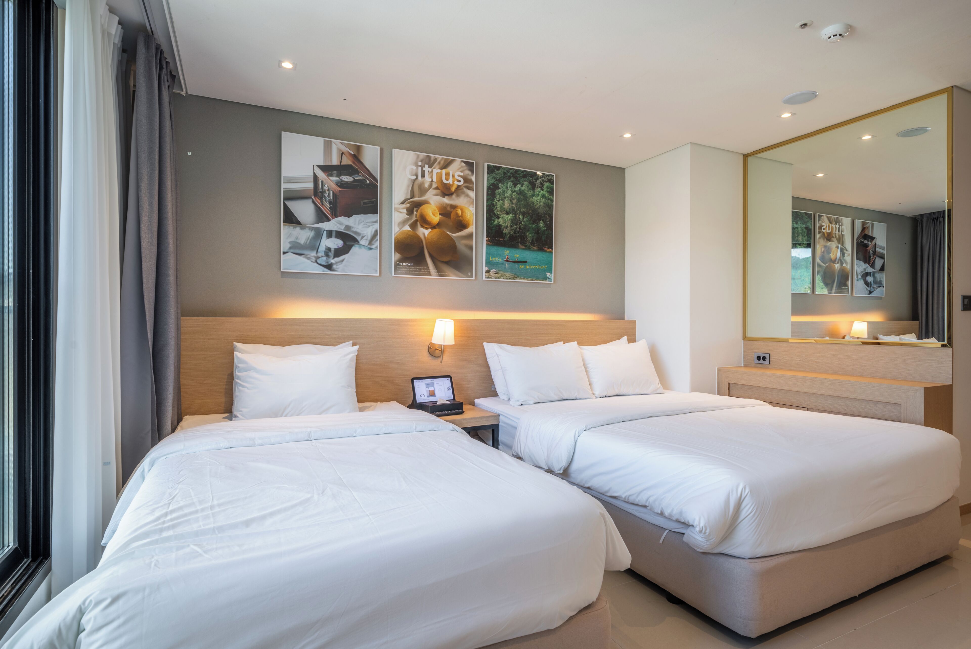 A hotel room with two beds, a desk with a laptop, a large mirror, and wall art.