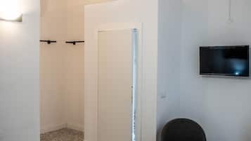 Un baño moderno con ducha, inodoro y lavamanos. Hay una silla y un televisor montado en la pared.