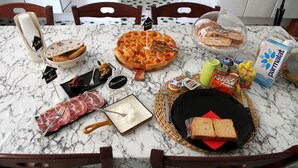 Uma mesa de mármore com pizza, pão, queijo e acompanhamentos.