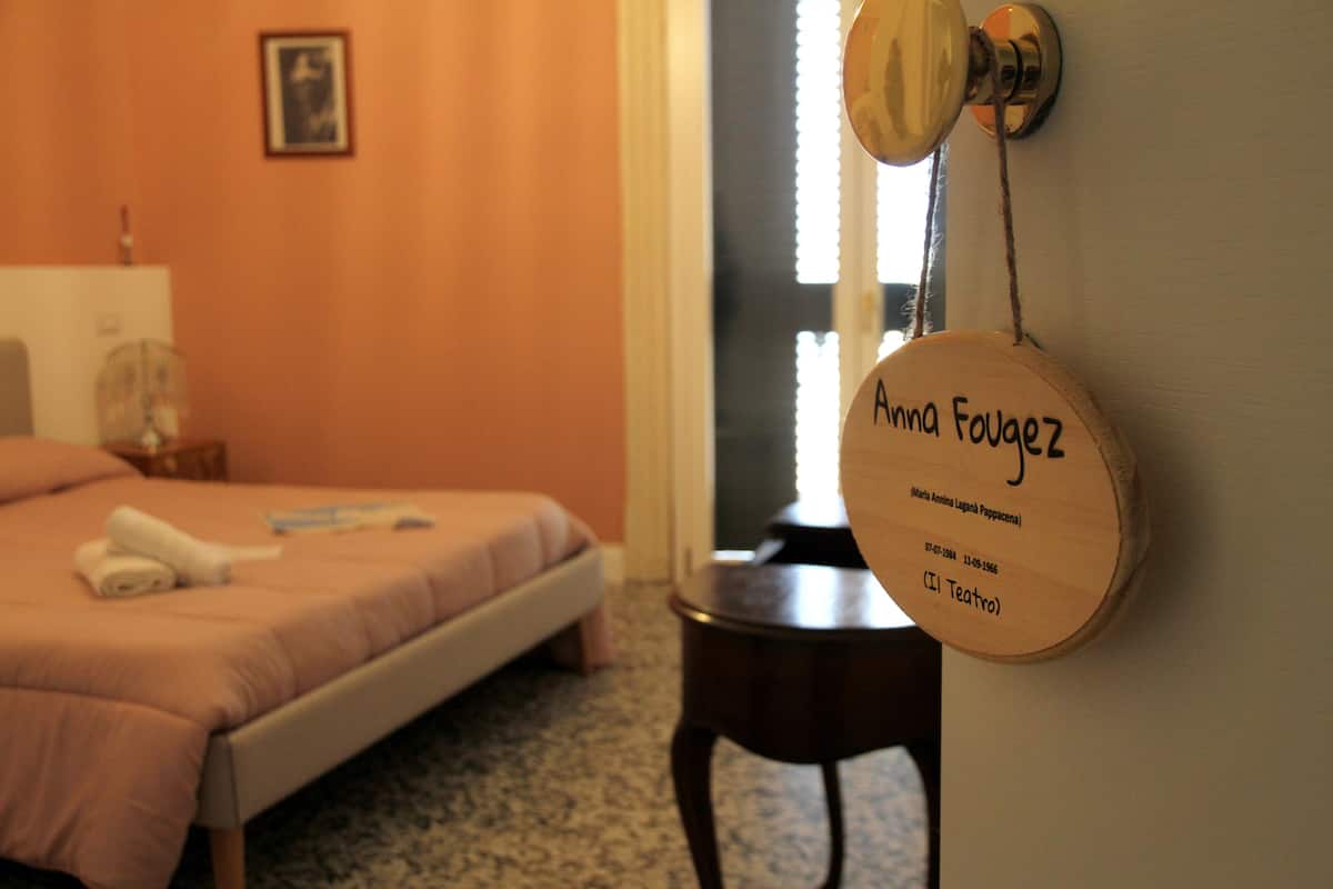 Habitación de hotel con cama, mesita de noche y lámpara de pared.