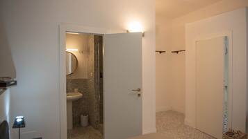 Un pasillo con una puerta de baño, una lámpara y un cubo de basura.