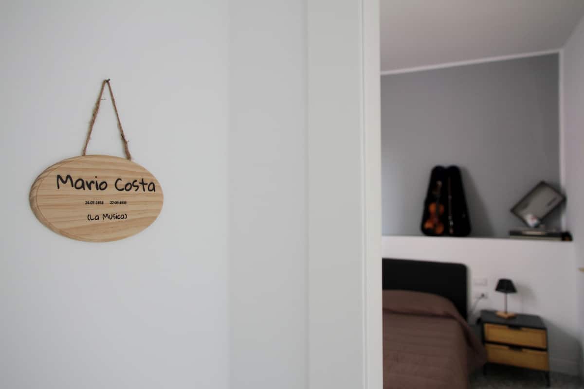 Una habitación con una cama, una mesita de noche, una lámpara y una guitarra en un estante.