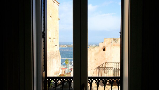 Vista da janela com varanda, com vista para a costa, edifícios e um corpo de água.