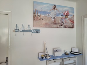 A wall with a calendar, a small sailboat, and a painting of a woman by the sea.