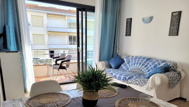 A modern living room with a sofa, a dining table with placemats, a potted plant, and a balcony with chairs. - OMEGA 4 2-C (Estartit)