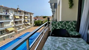 Un balcón con piscina, vista a edificios vecinos y un sofá estampado.