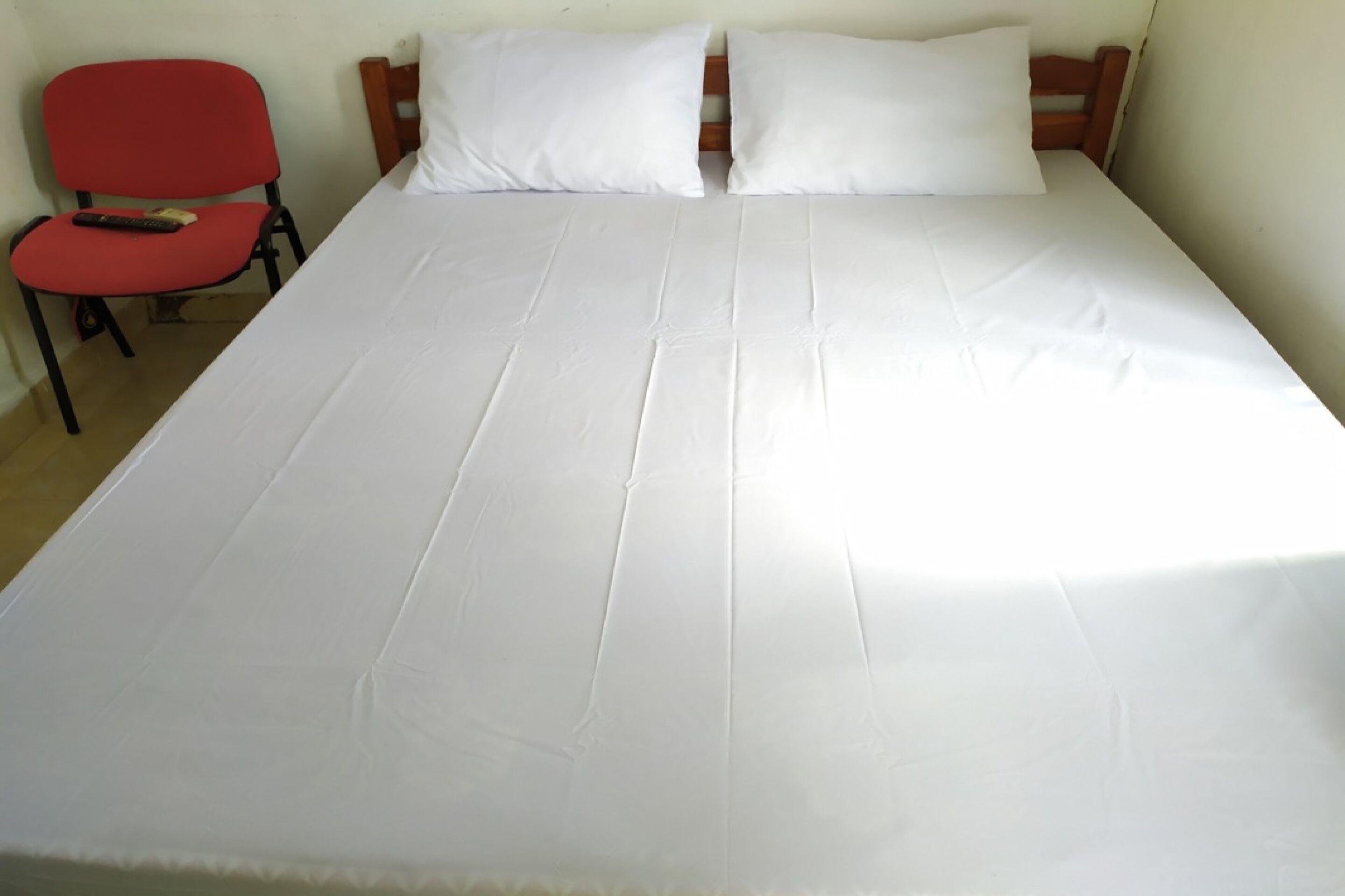 A bed with white sheets, a red chair, and a wooden headboard.
