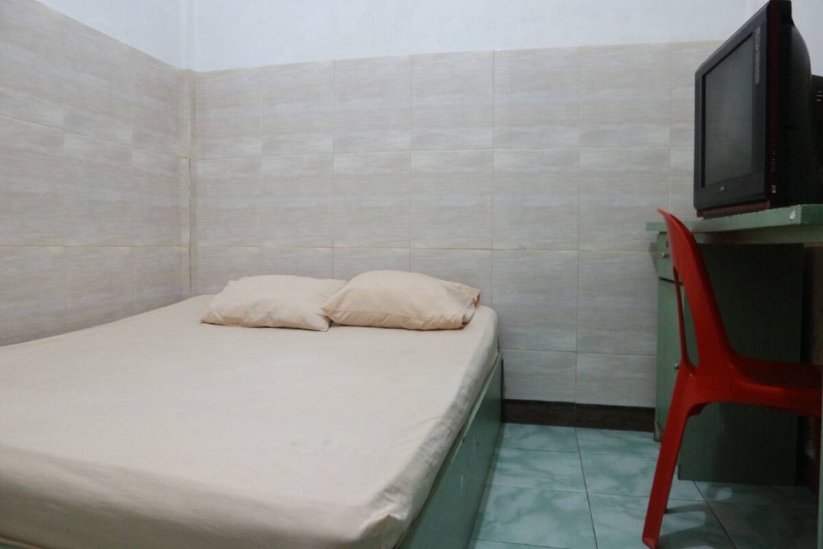 A small, single-bed room with a television on a stand and a red chair.