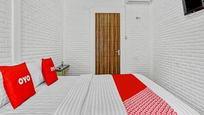 Habitación de hotel con paredes de ladrillo blanco, una puerta de madera, una cama con ropa blanca y roja, y un plaid rojo y blanco.